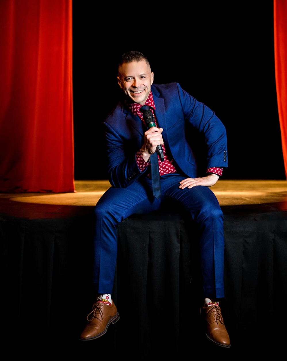 Erik Dominguez on stage with a microphone wearing a blue suit