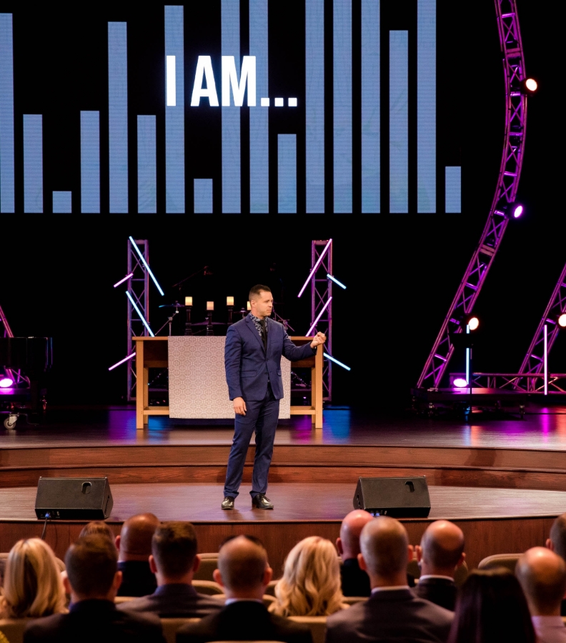 Erik Dominguez on stage with the words "I AM..." on screen behind him